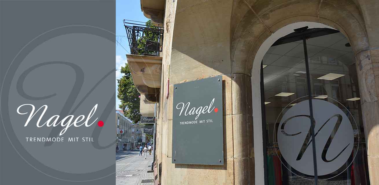 Ein Geschäftsschild mit der Aufschrift "Nagel. Trendmode mit Stil" hängt an einer Gebäudeaußenwand. Im Hintergrund ist eine Einkaufsstraße mit Passanten und Bäumen zu sehen.