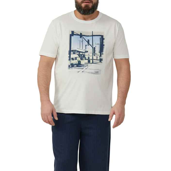 Ein Mann trägt ein weißes T-Shirt mit einem Straßenszene-Print, auf dem Autos und Ampeln zu sehen sind. Er steht in einem neutralen Studiohintergrund.